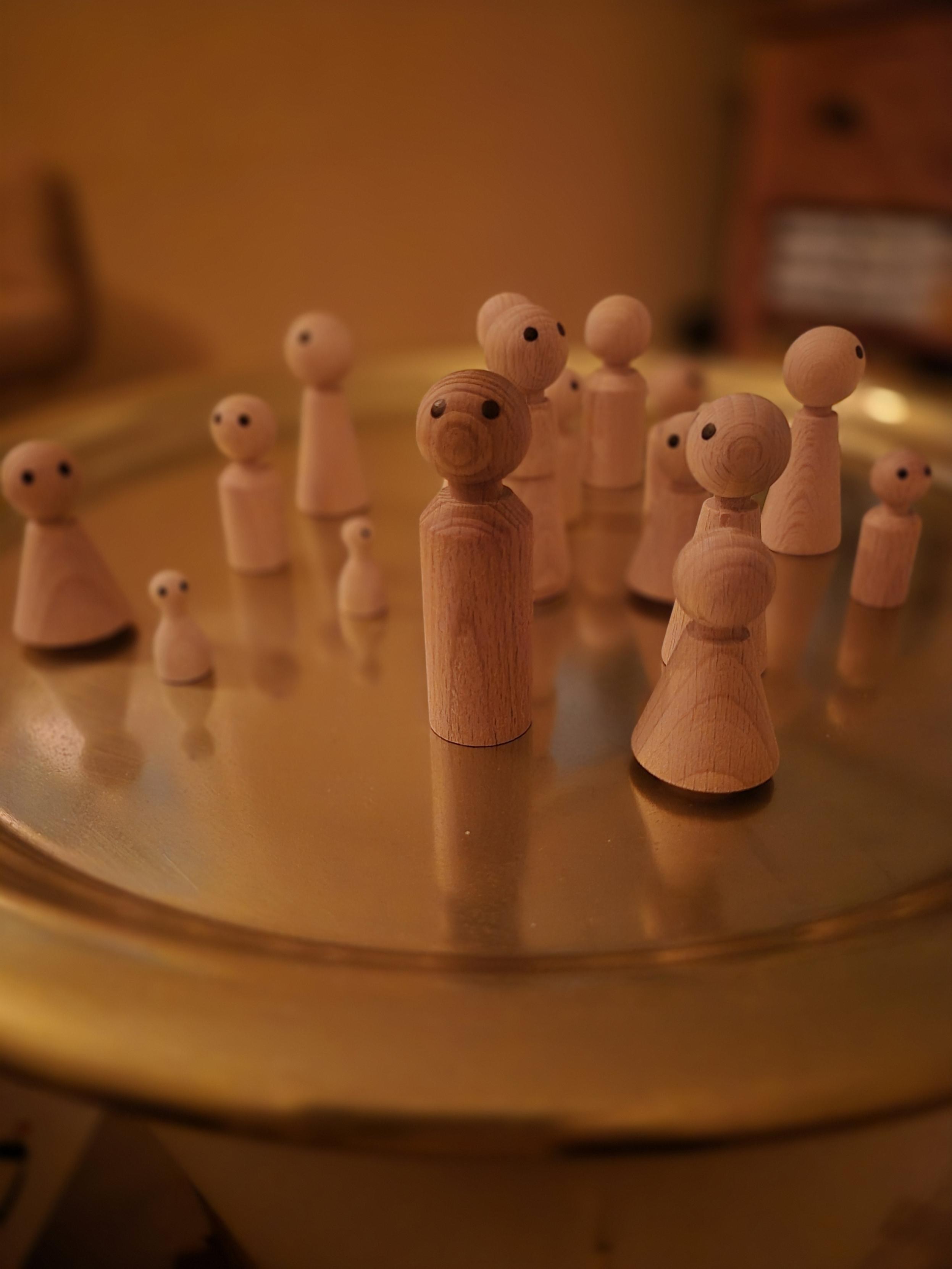 Houten figuurtjes op een gouden schaal — symbolisch voor onderlinge verbanden tijdens NEI-therapie.